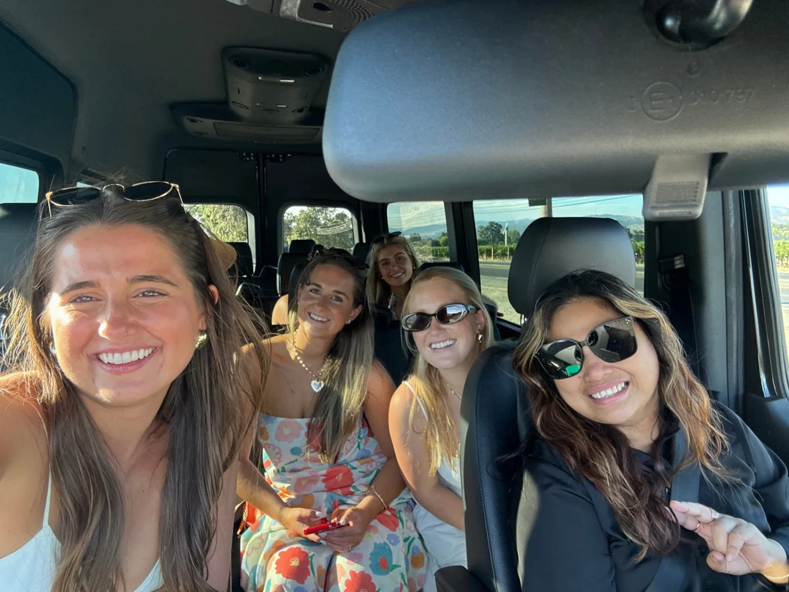 Five women smiling for a selfie inside a passenger vehicle.